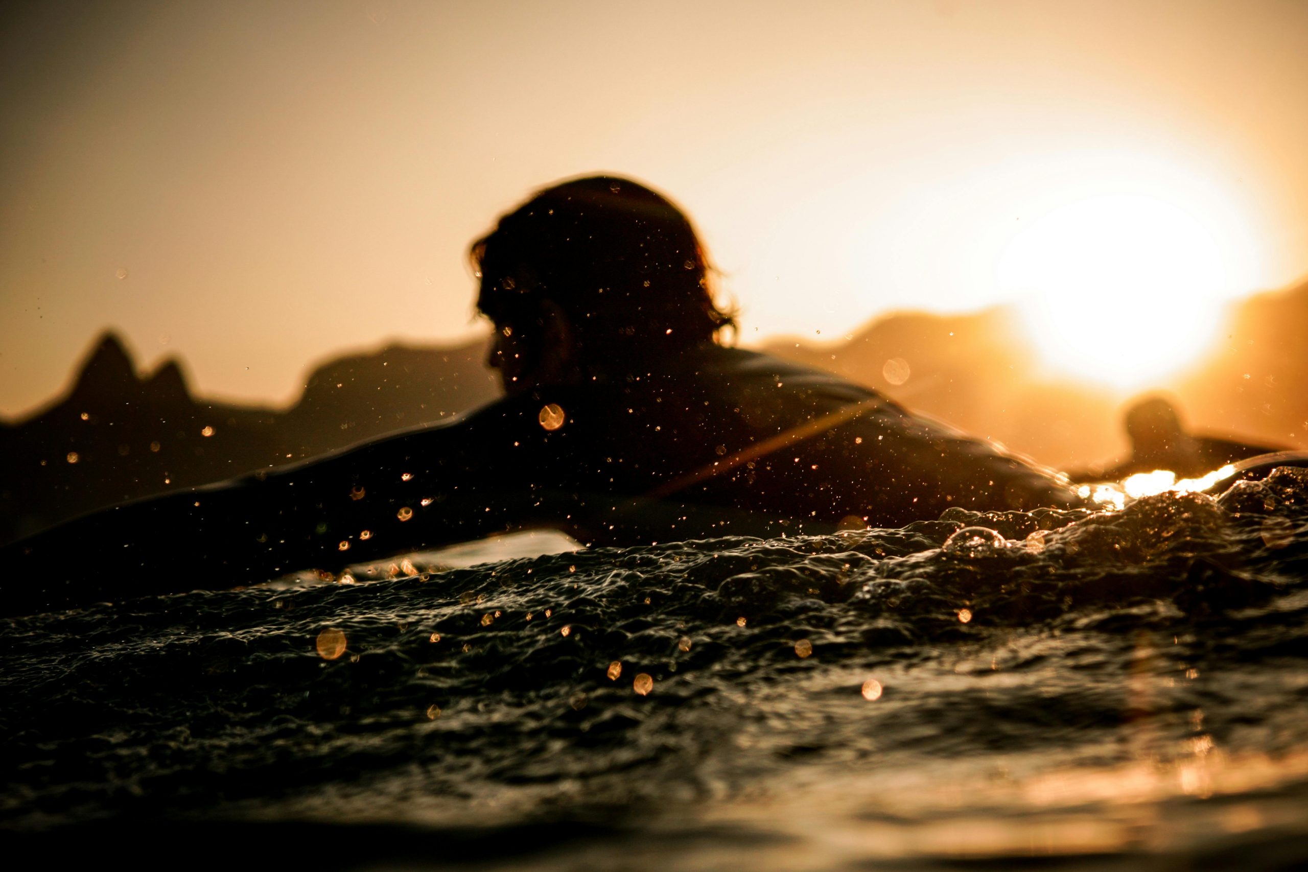 Silhouette of a surfer paddling during a vibrant Rio de Janeiro sunset.